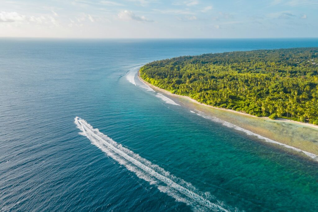 A small wooden speedboat crossing turquoise water toward a jungle-covered island near Perhentian, Malaysia